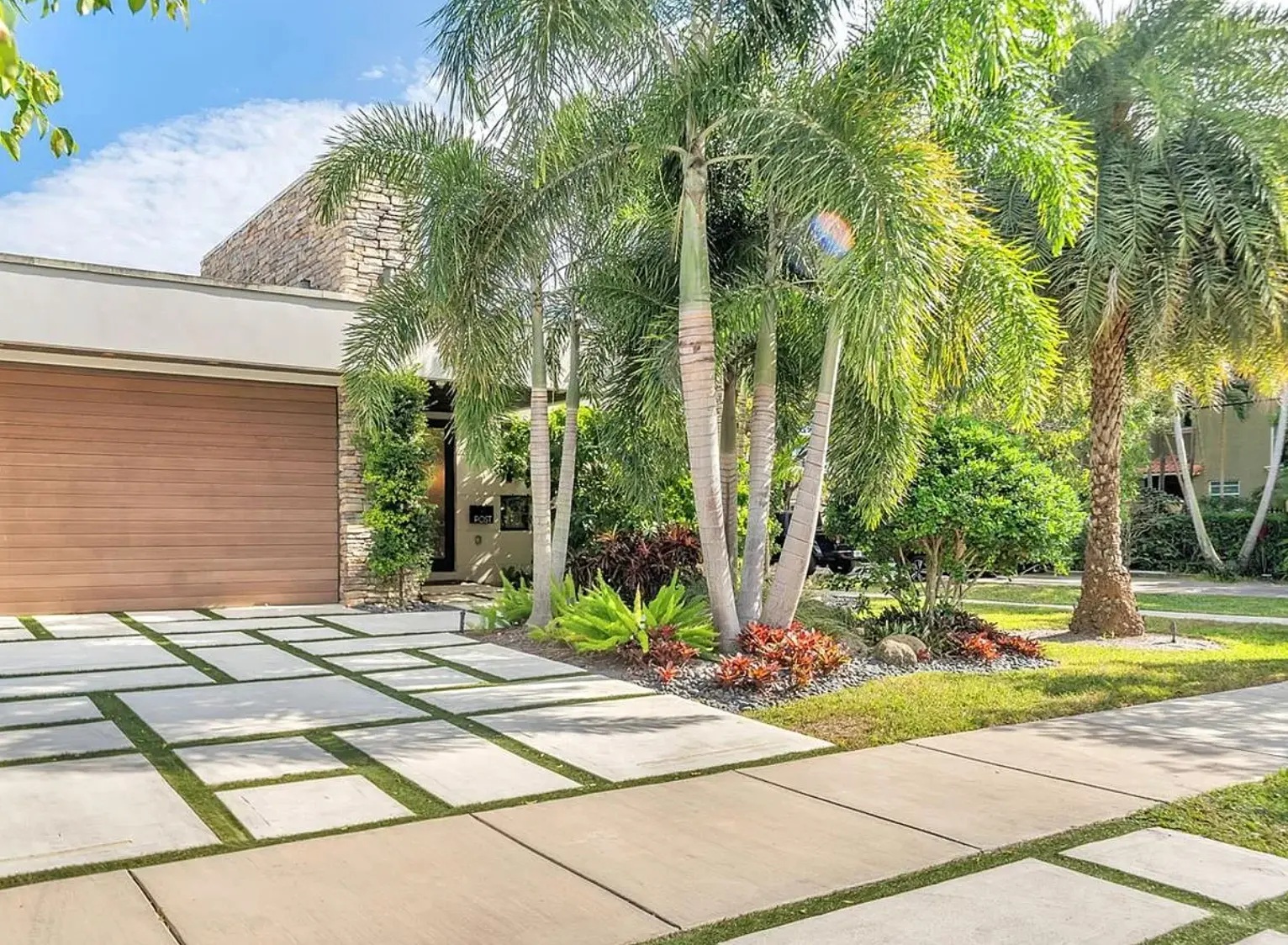 Contemporary home's entrance with tropical landscaping and a palm-lined driveway
